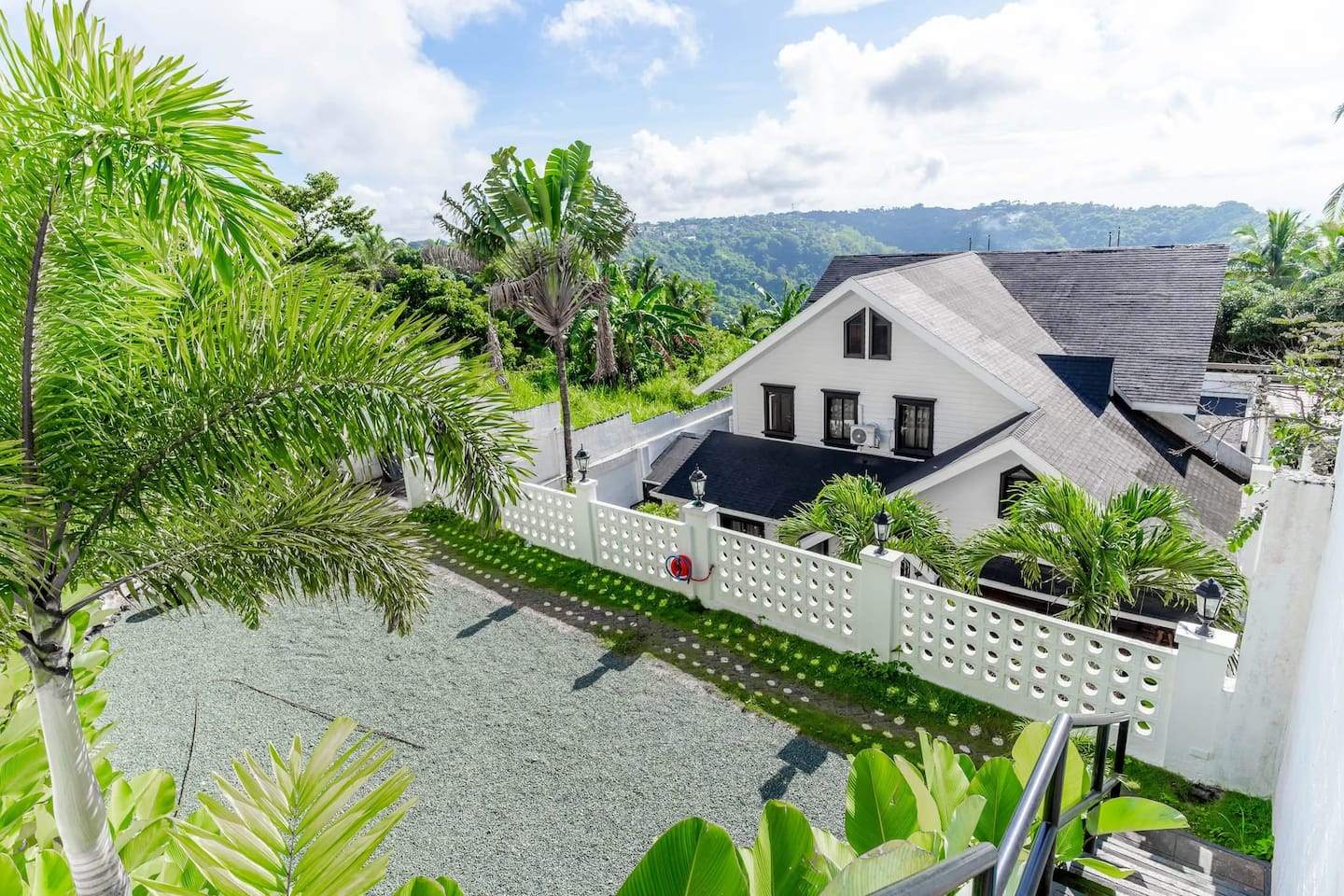 The villa from the road: a white gable house with black window frames, palms, and the Tagaytay ridge behind it