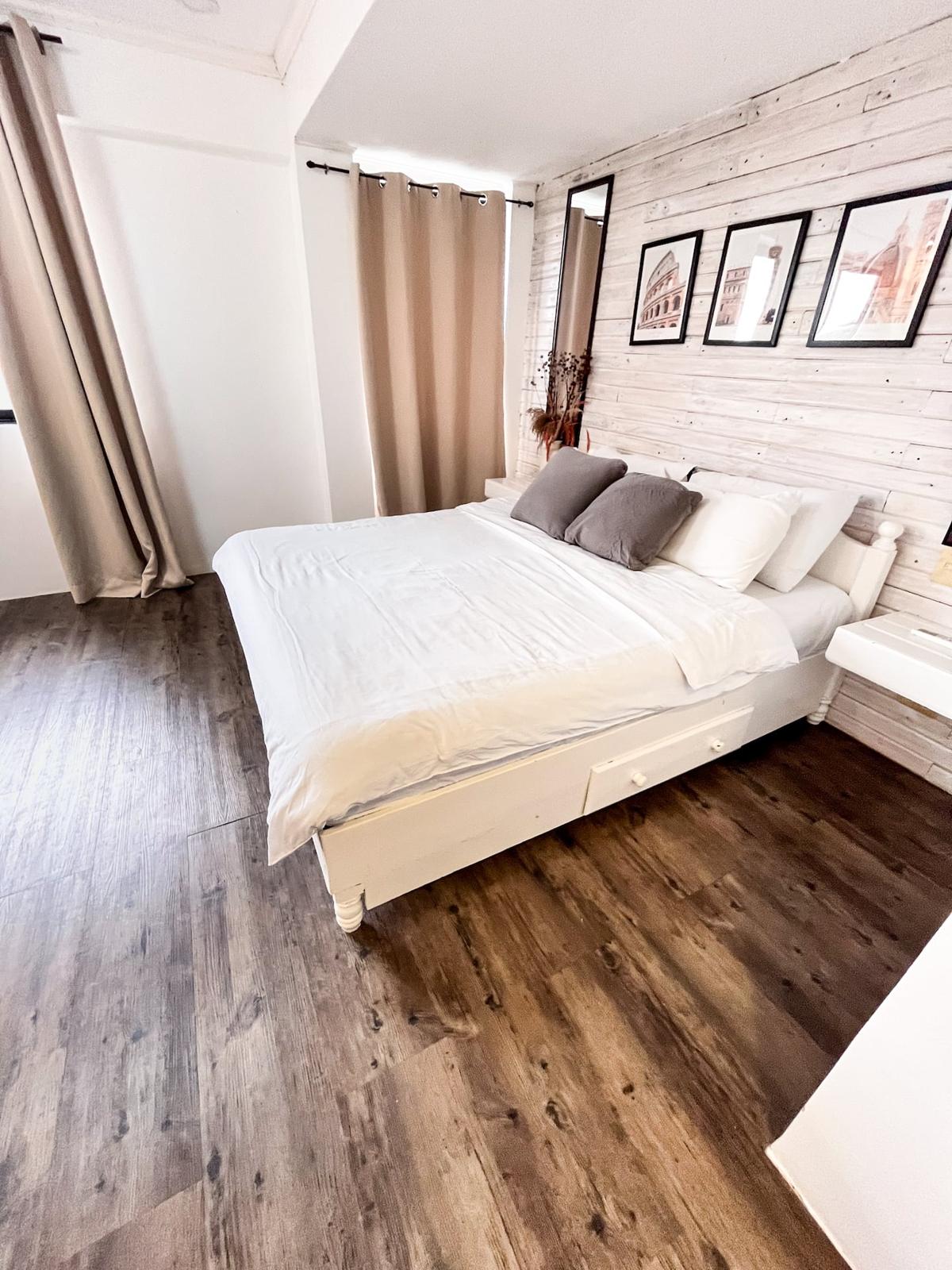 A bedroom with a white bed, wood floor and a whitewashed brick wall